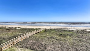 A beach with a wooden boardwalk leading to the shore. - Gulf-view Home w/ Dog Run in Surfside Beach! (Freeport)