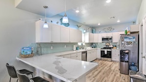 A modern kitchen with white cabinets, a marble island, black bar stools, and stainless steel appliances. - Gulf-view Home w/ Dog Run in Surfside Beach! (Freeport)