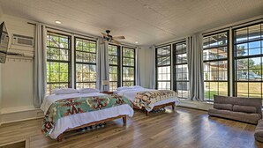 A spacious bedroom with two beds, large windows, a ceiling fan, and a wooden floor.
