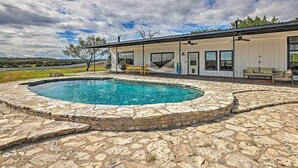 A modern house with a swimming pool surrounded by stone tiles, large windows, and a hammock.