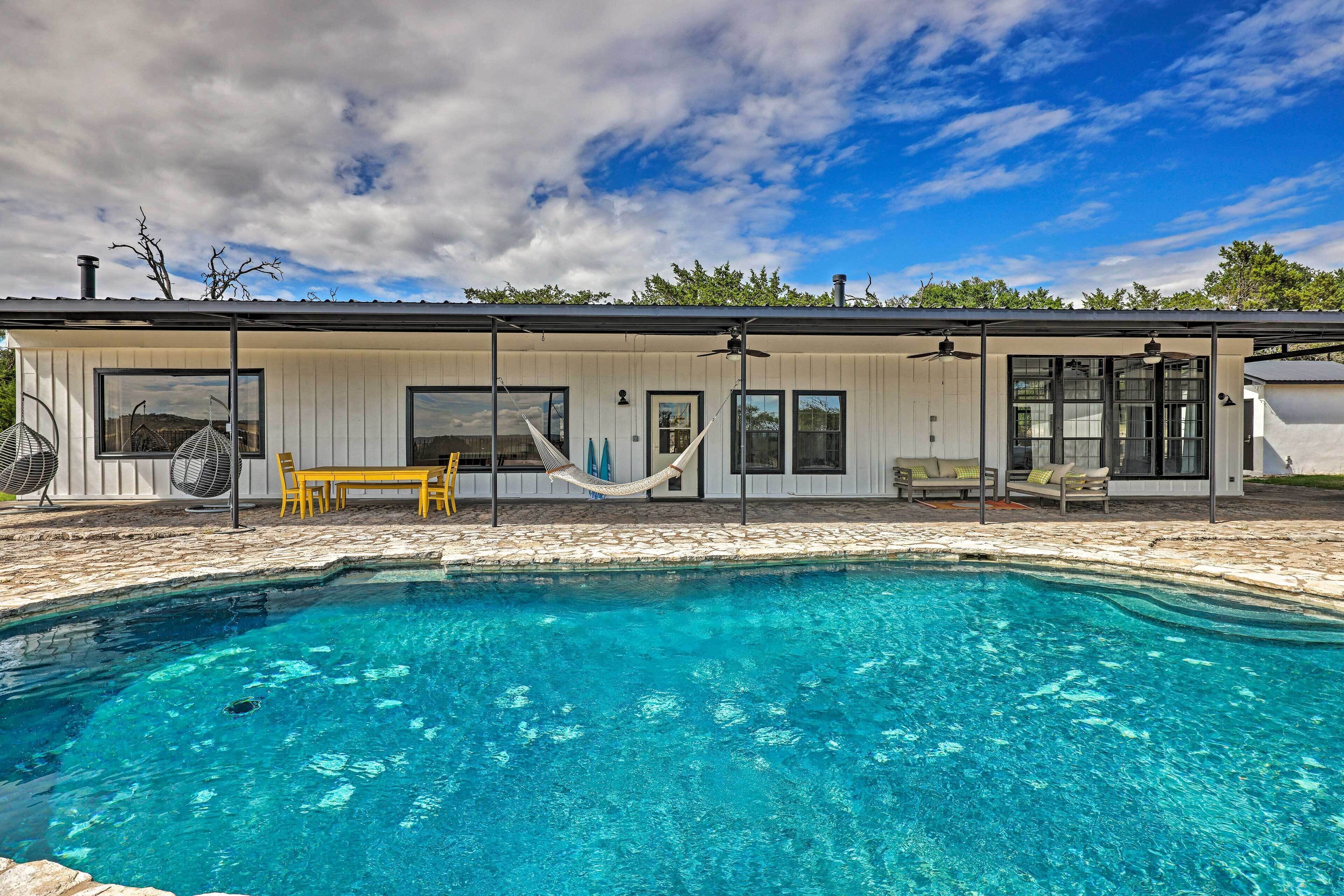 Una casa moderna con piscina, muebles de exterior y una hamaca.