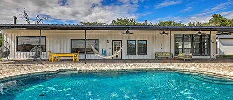 Una casa moderna con piscina, muebles de exterior y una hamaca.