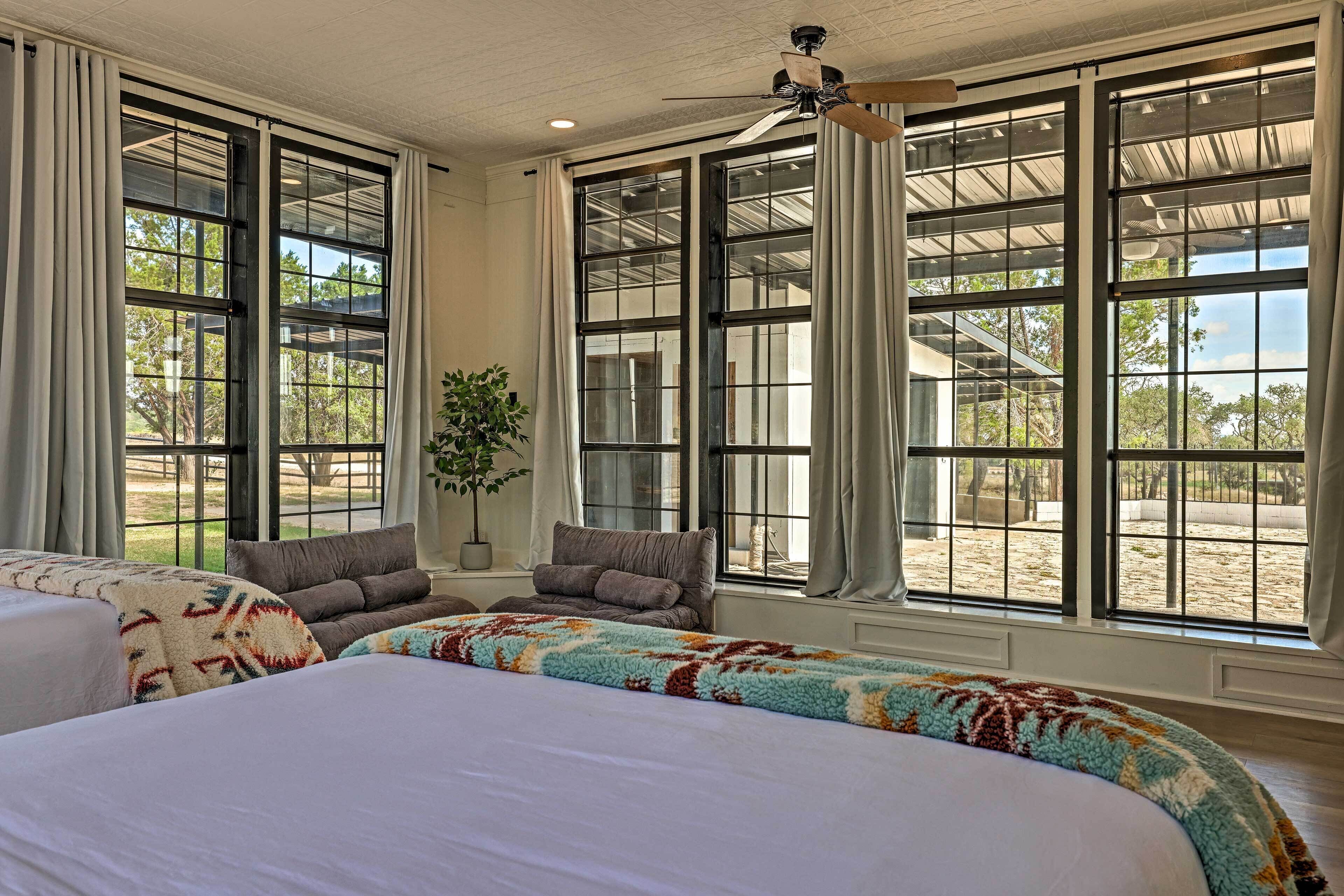 A spacious bedroom with large windows, a ceiling fan, and a bed with a colorful blanket.