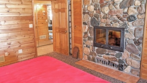 Interior de una cabaña de troncos con chimenea de piedra, paredes de madera y alfombra roja.