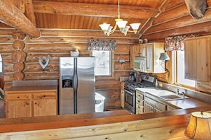A log cabin kitchen with wooden cabinets, a stainless steel refrigerator, a stove, and a sink.