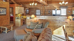 Interior de una cabaña de troncos con una sala de estar acogedora, una cocina con refrigerador y una mesa de comedor.