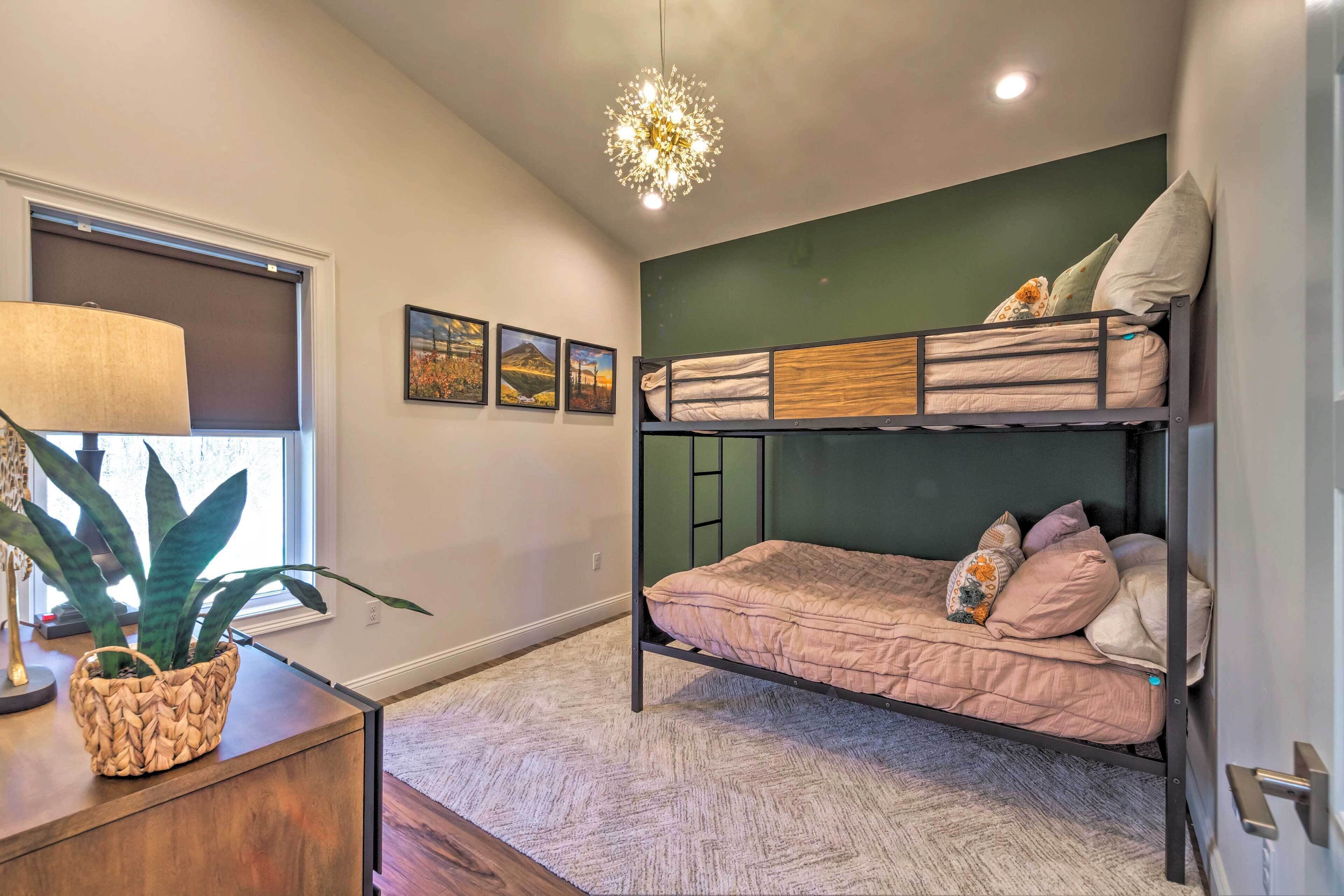 A modern bedroom with a bunk bed, a large potted plant, a lamp, and framed pictures on the wall.