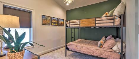 A modern bedroom with a bunk bed, a large potted plant, a lamp, and framed pictures on the wall.