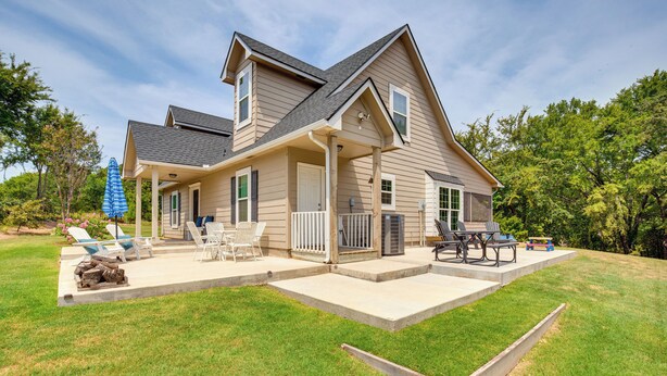 Ein zweistöckiges Haus mit einer Veranda, einer Terrasse mit Gartenmöbeln und einem gepflegten Rasen.