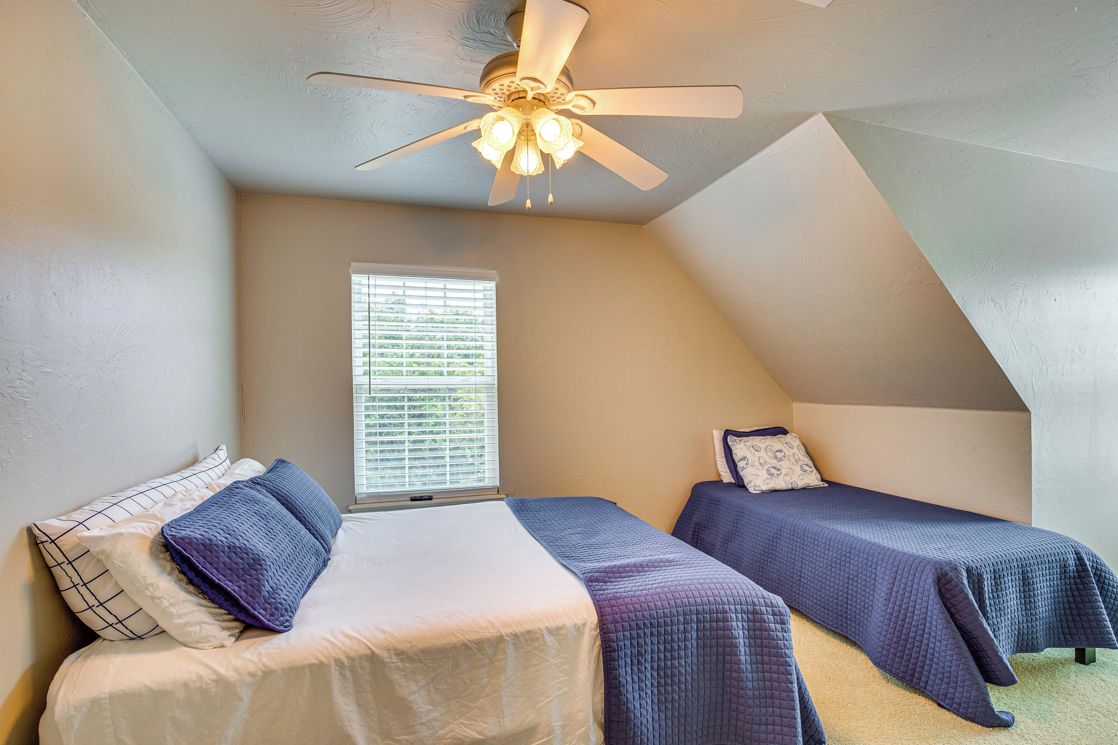 Une chambre avec deux lits simples, un ventilateur de plafond et une fenêtre avec des stores.