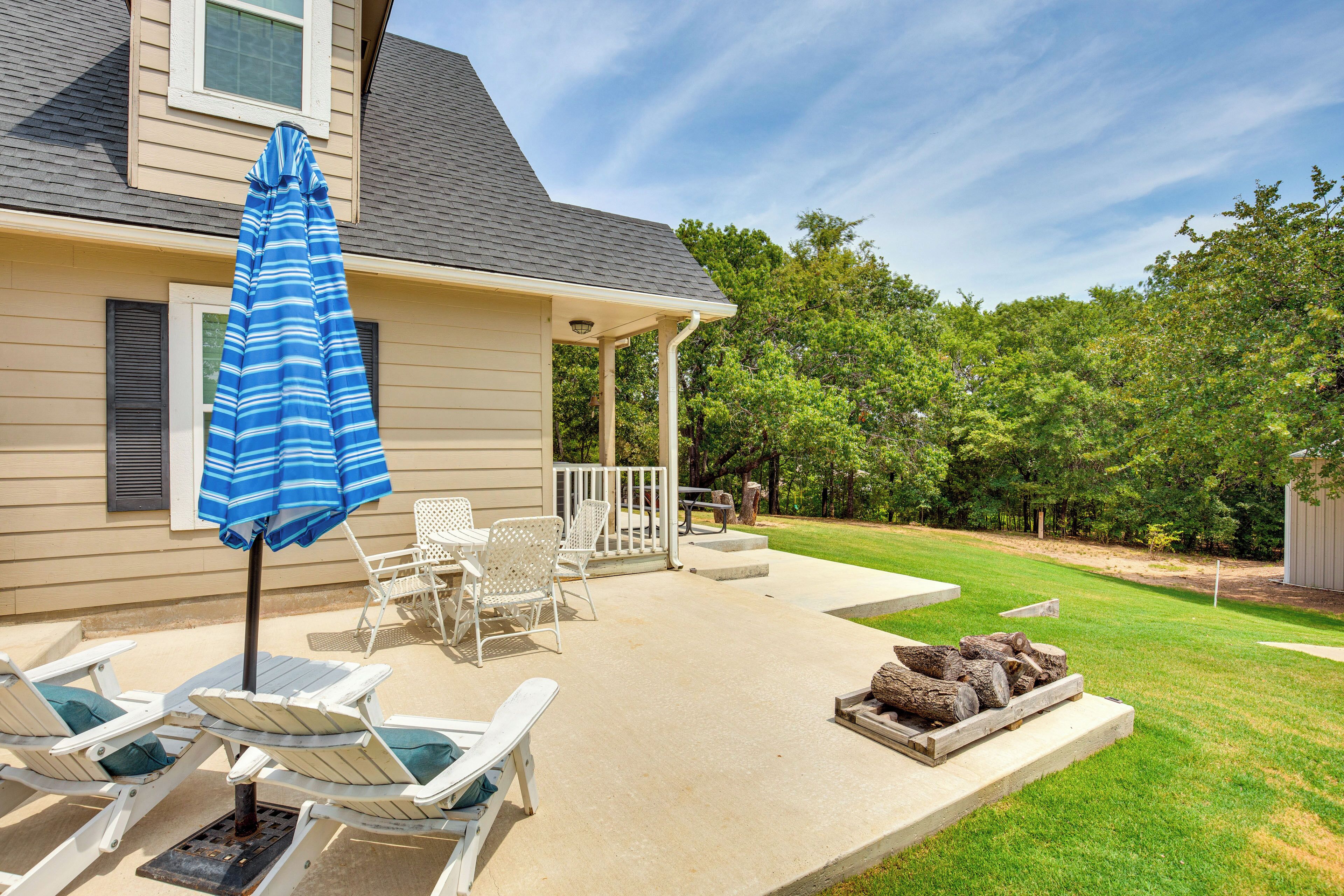 A covered patio with lounge chairs and a striped umbrella, a fire pit, and a well-maintained lawn.