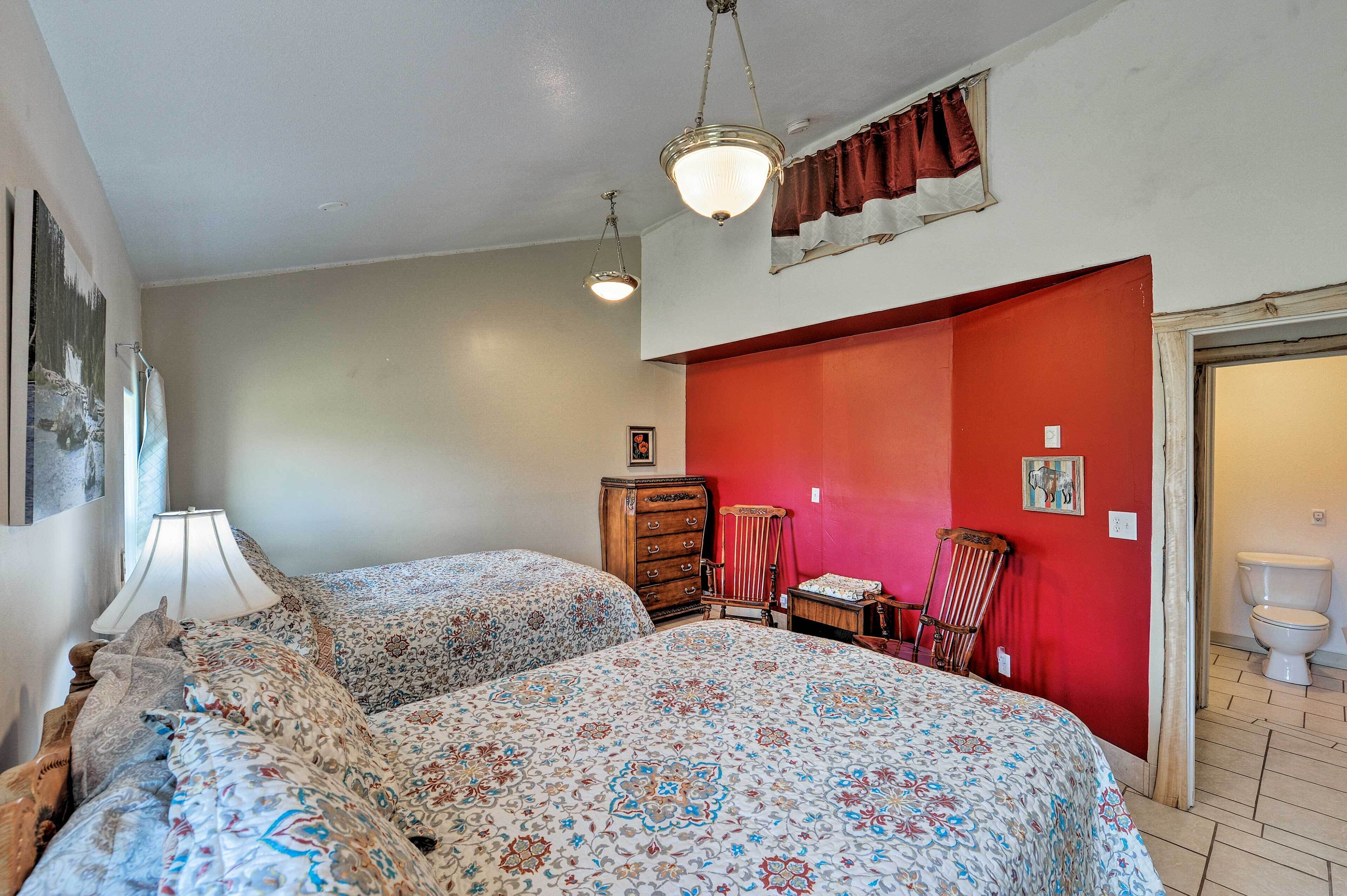 A bedroom with two beds, a dresser, a chair, and a red accent wall.