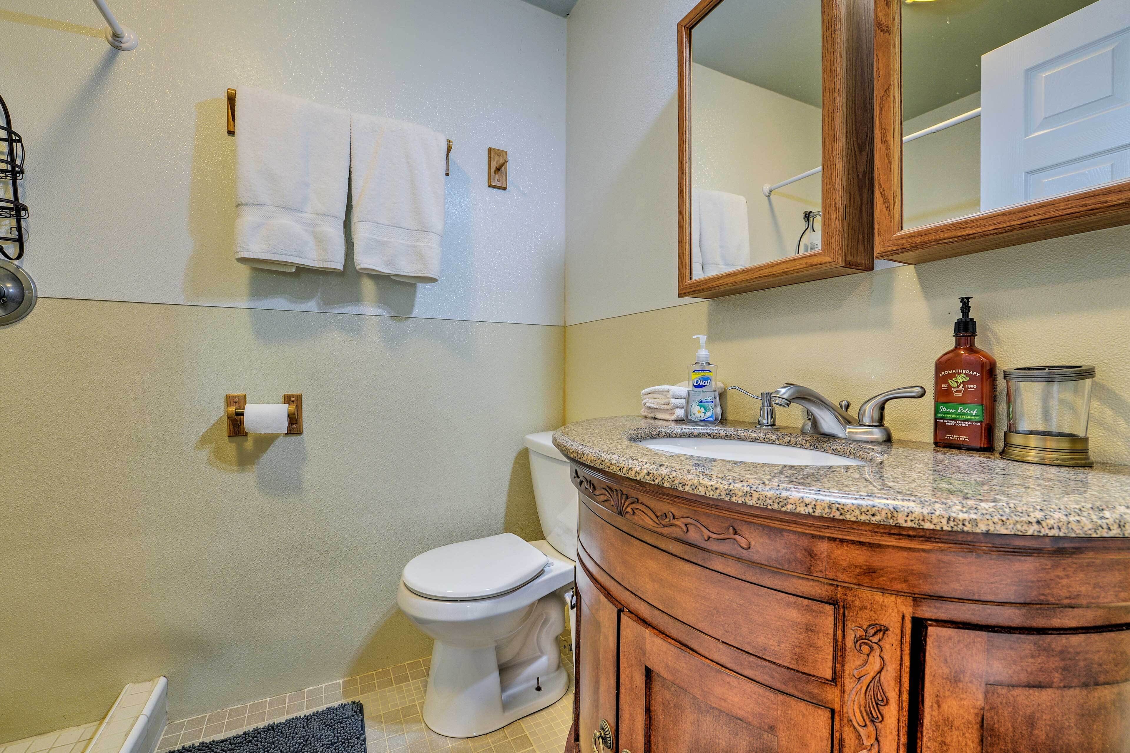 A bathroom with a toilet, sink, and mirror. There are towels hanging on the wall and a soap dispenser on the sink.