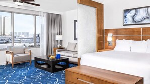 Quarto de hotel com cama grande, escrivaninha, cadeira, mesa de centro e vista da cidade.