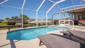 A swimming pool with a covered area, lounge chairs, and a view of houses in the background.
