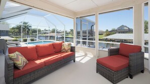 A sunroom with a large window, a pool, and outdoor furniture.