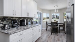 A modern kitchen with white cabinets, granite countertops, and a dining area with wooden chairs and a table.