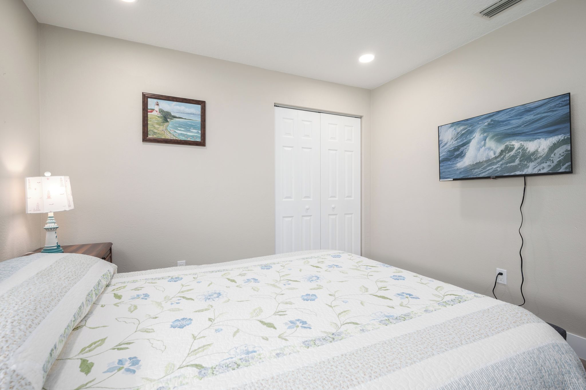 Une chambre à coucher avec un lit, une table de chevet, une lampe, une porte et un tableau au mur.