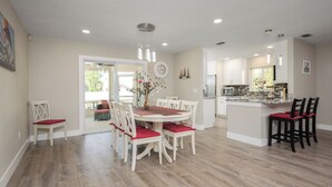 A spacious kitchen with white cabinets, a central island, and a dining area with white chairs and a red tablecloth.