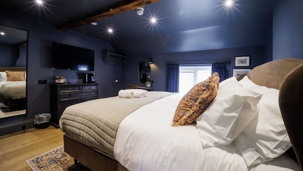 A bedroom with a large bed, a dresser, a mirror, and a window with curtains. - The Silk Rooms at Freemasons Inn (Knutsford)