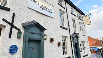A building with a sign for 'The Six Rooms' pub, a traditional design with a green door, and outdoor seating with red chairs.