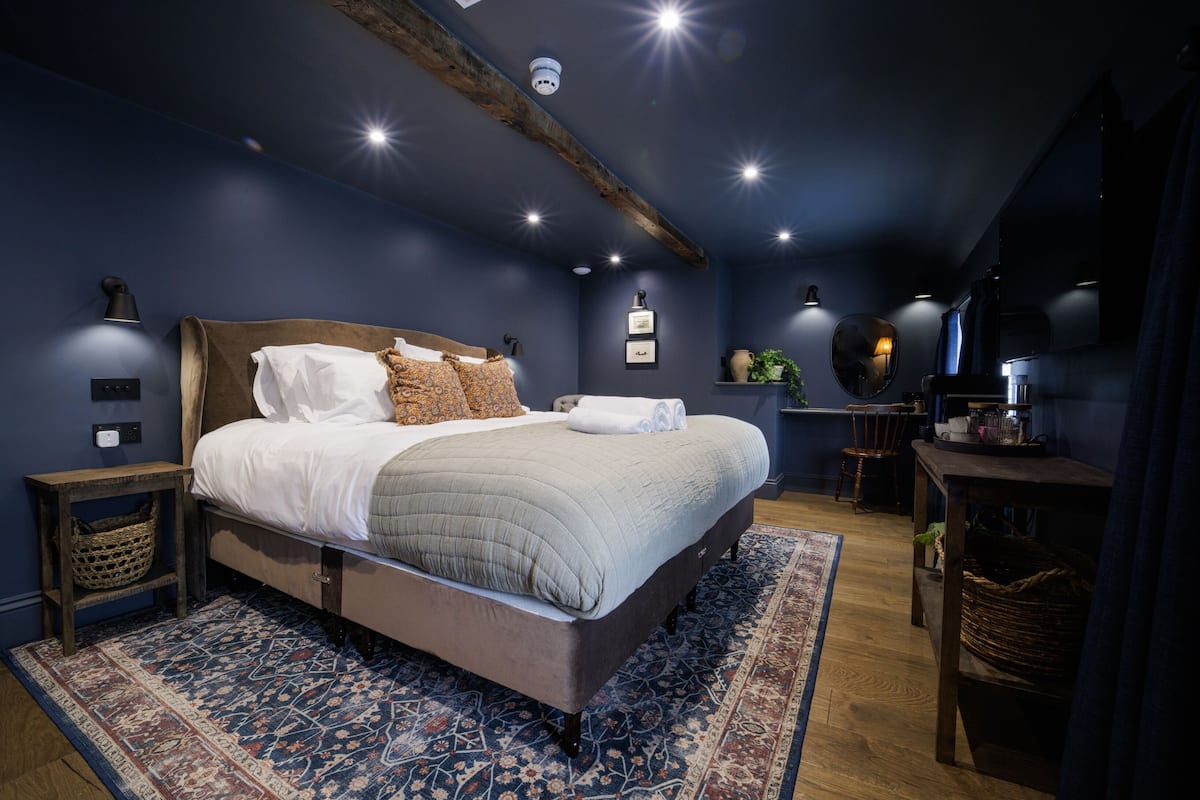 Ein Schlafzimmer mit einem großen Bett, einem Holzkopfteil, einem gemusterten Teppich und einer Decke mit freiliegenden Balken.