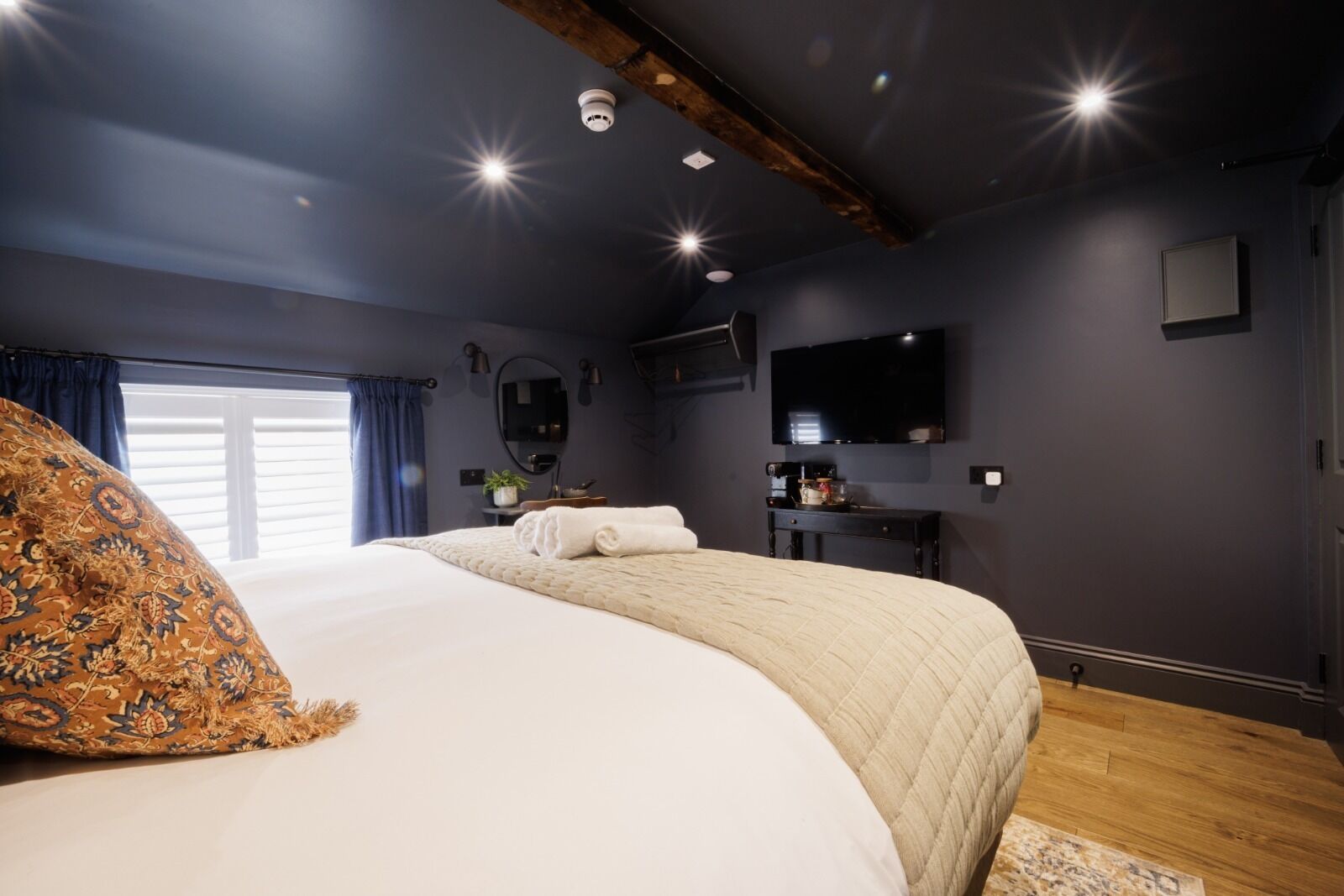 Un dormitorio moderno con una cama grande, un televisor de pantalla plana, una lámpara empotrada en el techo y una viga de madera.