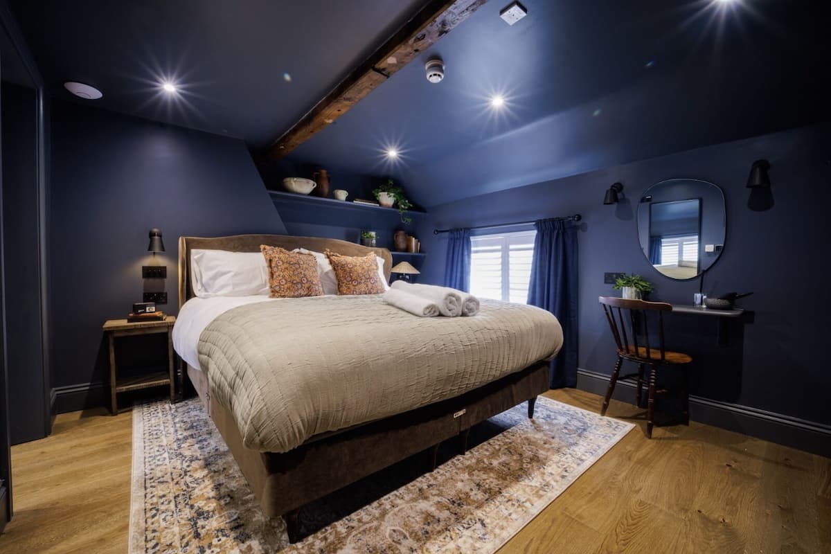 Ein Schlafzimmer mit einem großen Bett, einem Nachttisch, einem Sessel, einem Schreibtisch und einem Spiegel.