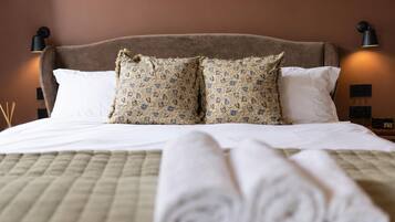 Una cama bien hecha con un edredón acolchado, dos almohadas estampadas y toallas blancas enrolladas.