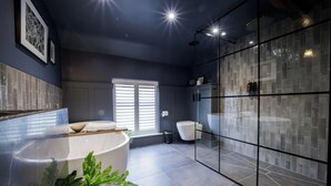 A modern bathroom with a large bathtub, a glass shower enclosure, and a window with blinds. - The Silk Rooms at Freemasons Inn (Knutsford)