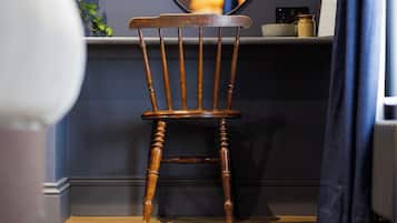 Una silla de madera con respaldo alto y patas torneadas, ubicada frente a una pared oscura con un estante encima.