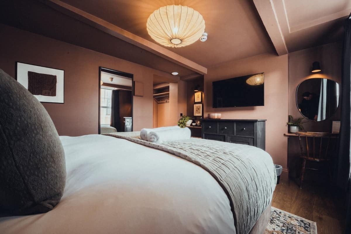 Ein modernes Hotelzimmer mit einem großen Bett, einem Flachbildfernseher, einem Schreibtisch mit Stuhl und einem großen Spiegel.