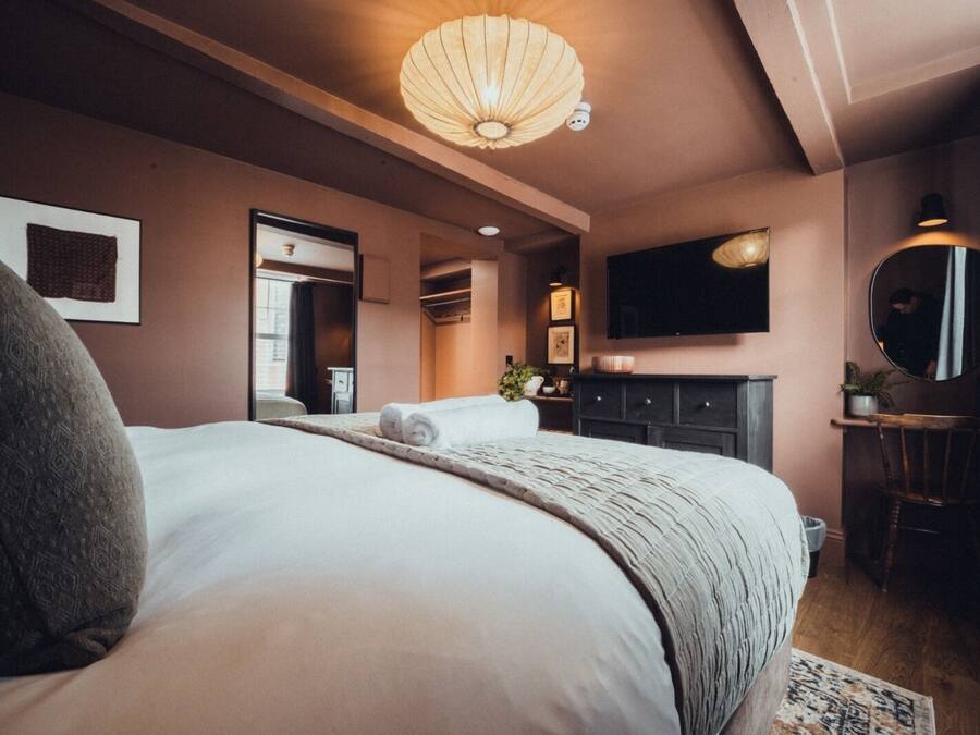 A modern hotel room with a large bed, a flat-screen TV, a desk with a chair, and a large mirror.