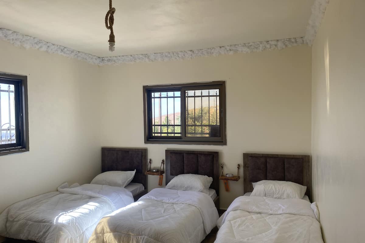 A room with three single beds, a window with bars, and a hanging light fixture.