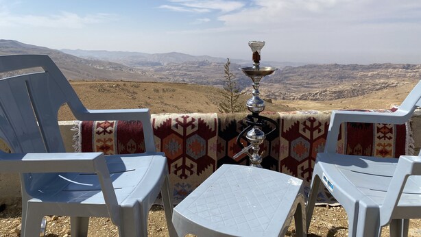 A terrace with two white plastic chairs and a small table, overlooking a mountainous landscape. - Nabati Hostel  (At-Taybeh)
