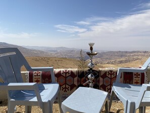 A terrace with two white plastic chairs and a small table, overlooking a mountainous landscape.