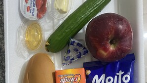A tray with a hot dog, a banana, a packet of Minto chocolate hazelnut, a packet of orange juice, a cucumber, a strawberry yogurt, and a small container of butter. - Nabati Hostel  (At-Taybeh)