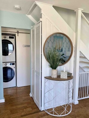 A laundry room with two washing machines, a mirror, and a small table with decorative items.