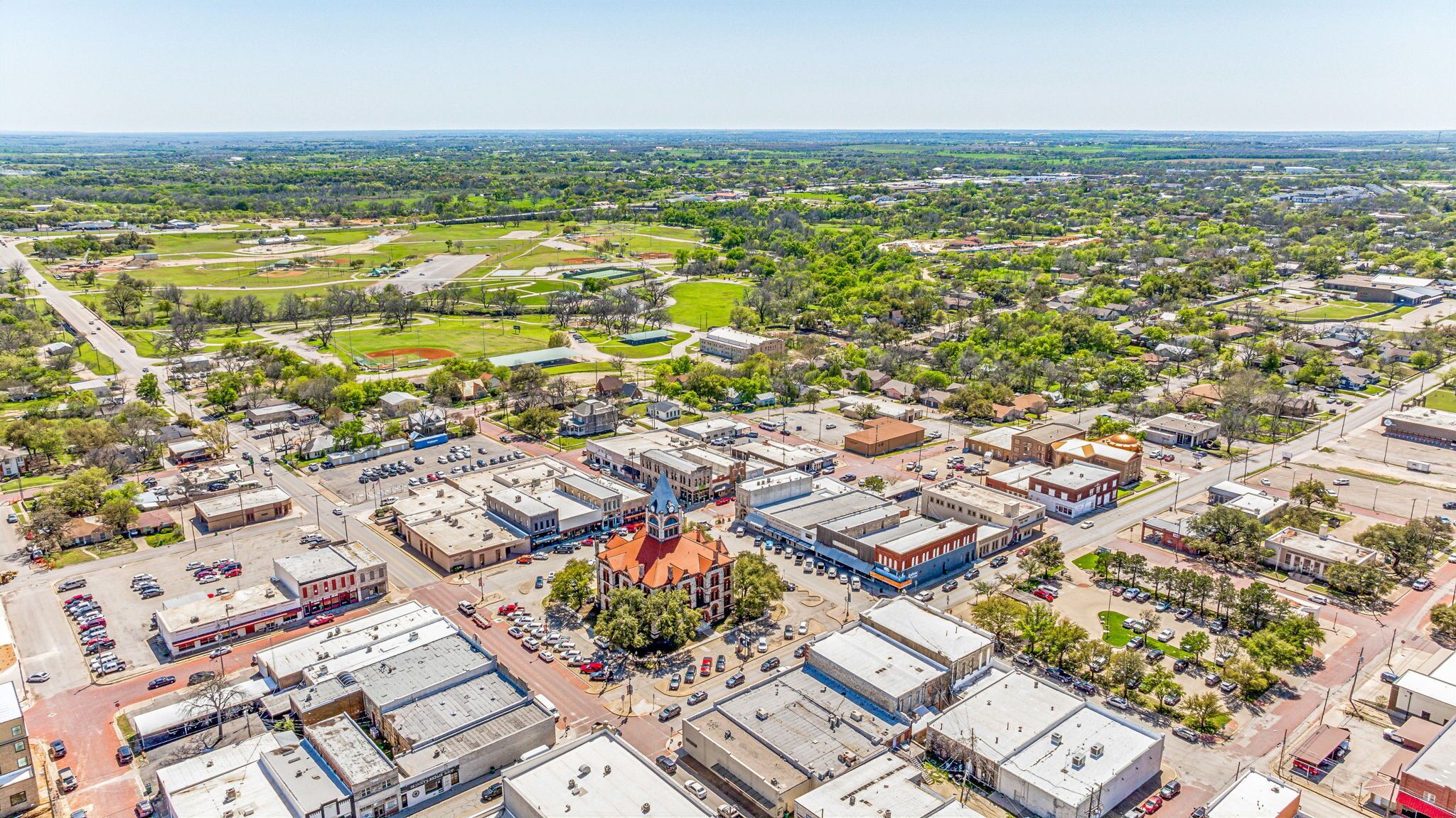 Vista aérea de un pueblo con una plaza central, edificios circundantes y zonas verdes.