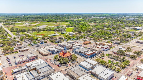 An aerial view of a town with a central square, surrounding buildings, and green spaces.
