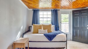 Een slaapkamer met een houten plafond, een bed met wit beddengoed, een klein houten tafeltje en een donkere deur.