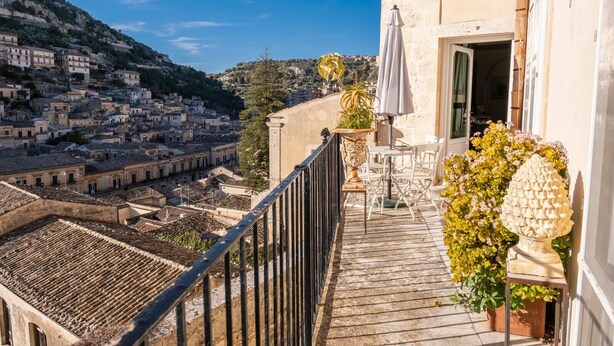 A balcony with a view of a cityscape, a table with chairs, and a potted plant. - Jasmine Luxury House with terrace (Modica)
