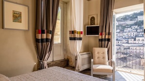 A bedroom with a bed, a chair, a television, and a view of a town through a window. - Jasmine Luxury House with terrace (Modica)