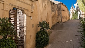 A narrow cobblestone street with a gate and a building with a textured wall. - Jasmine Luxury House with terrace (Modica)
