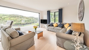 A spacious living room with a large window offering a scenic view, a comfortable sofa set, and a flat-screen TV. - Beach View (Ilfracombe)