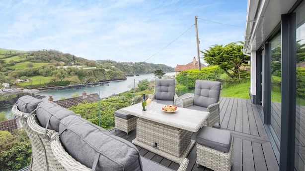 A deck with wicker furniture and a table, overlooking a river and hills. - Beach View (Ilfracombe)