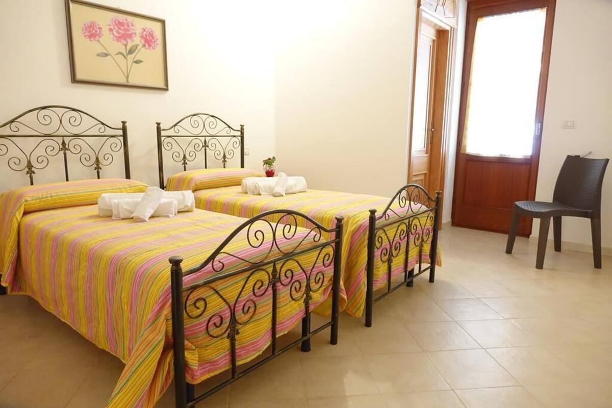 Quarto com duas camas, uma cadeira e porta que dá para o exterior.