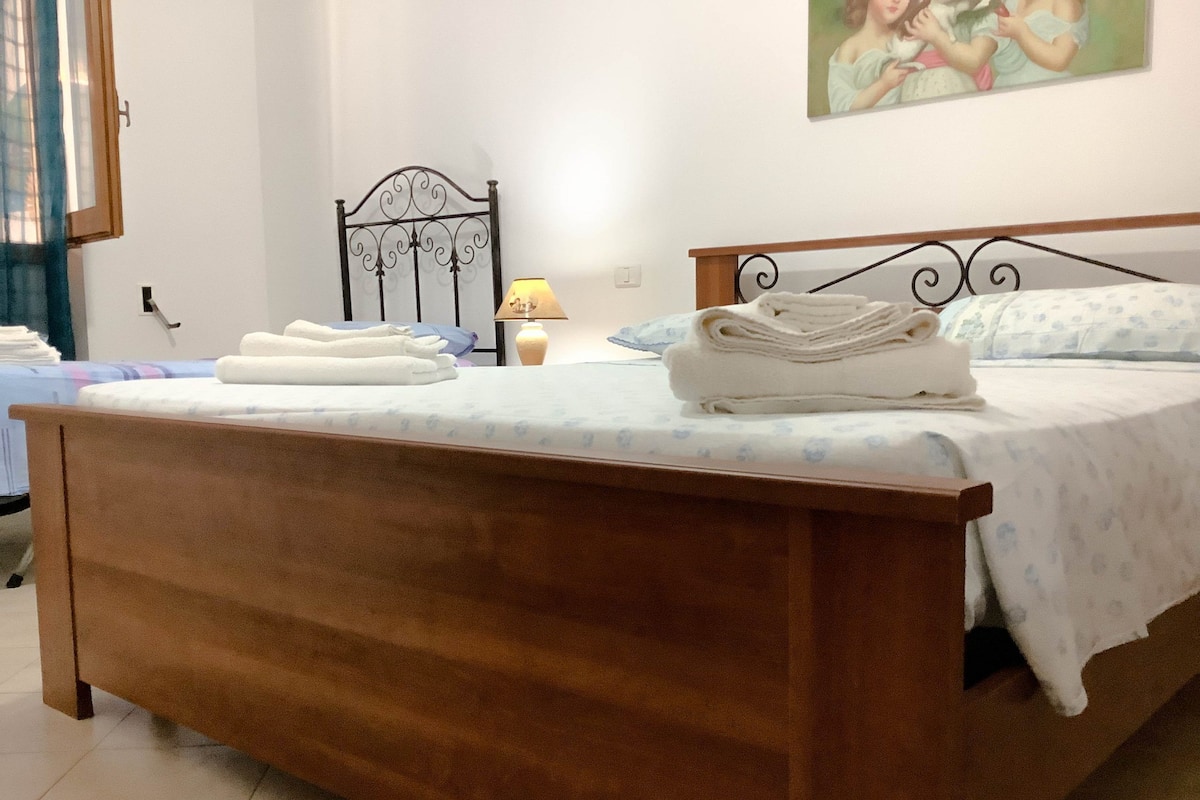 Quarto com cama de madeira, almofadas e toalhas dobradas.