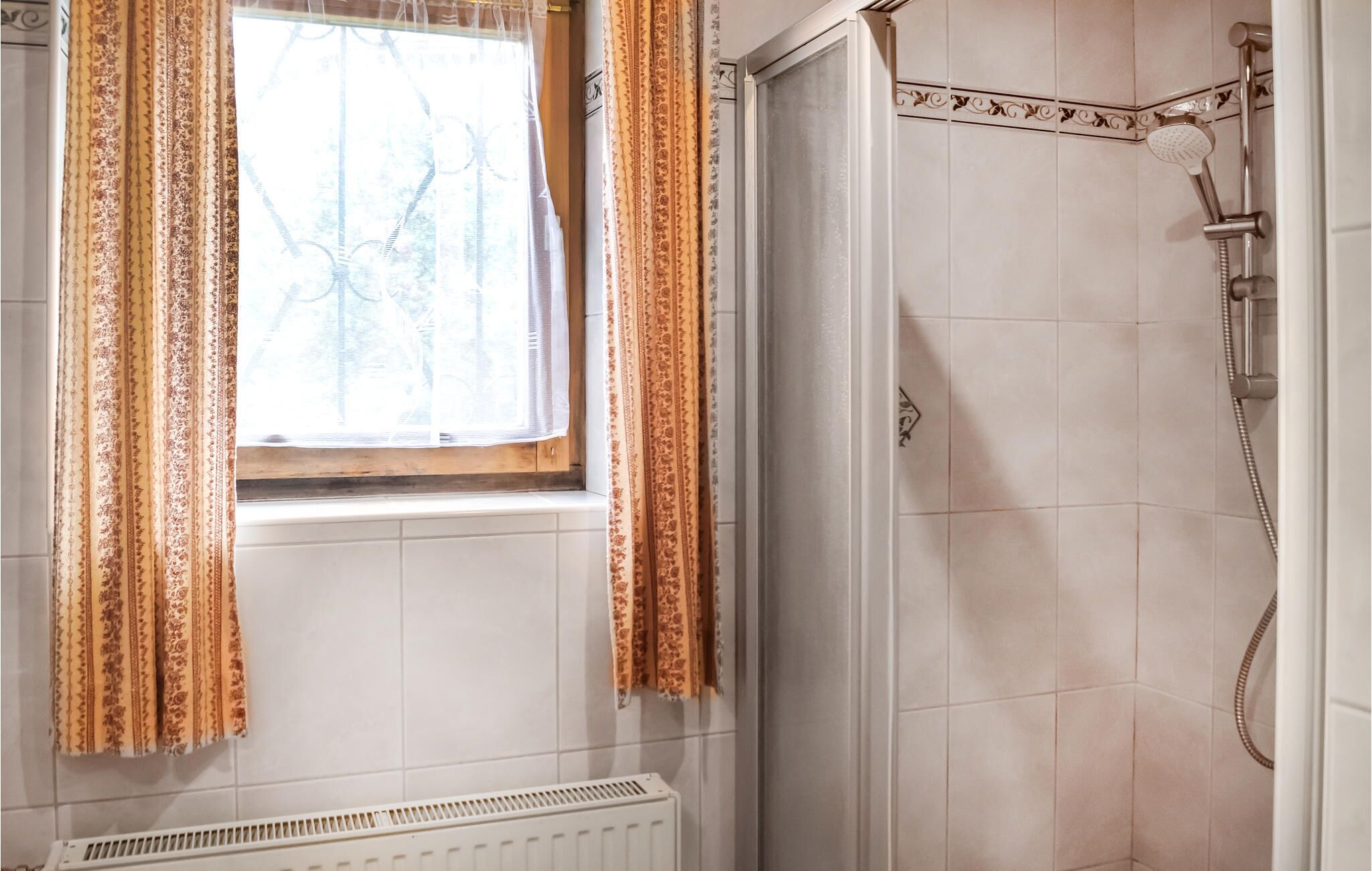Ein Badezimmer mit Fenster, Heizkörper und Duschbereich.