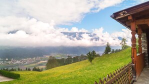 Une vue pittoresque depuis un balcon en bois donnant sur une vallée, avec une montagne en arrière-plan.